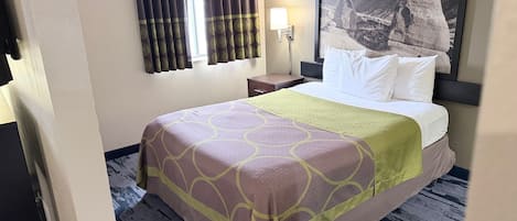 Una habitación de hotel con una cama, una mesita de noche, una lámpara y un ventanal con cortinas.
