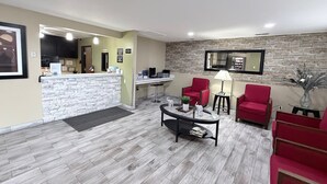 A reception area with a stone counter, red chairs, a small table with a lamp, and a mirror on the wall. - Super 8 by Wyndham Logan (Logan)