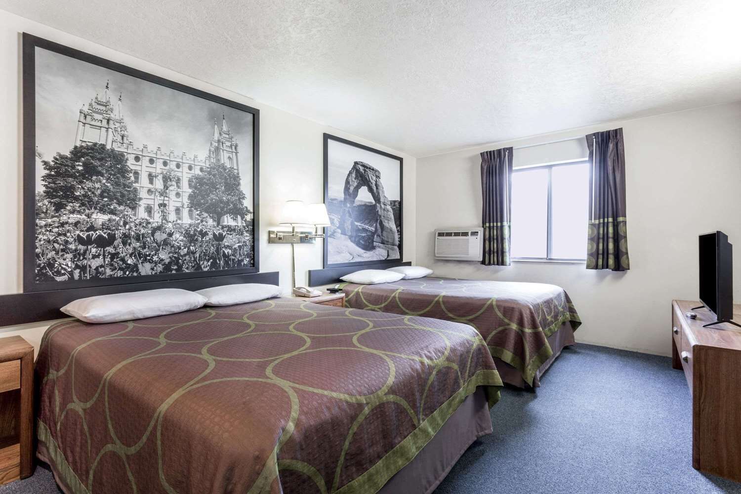Ein Hotelzimmer mit zwei Betten, einem großen gerahmten Foto, einem Fernseher und einem Fenster mit Vorhängen.