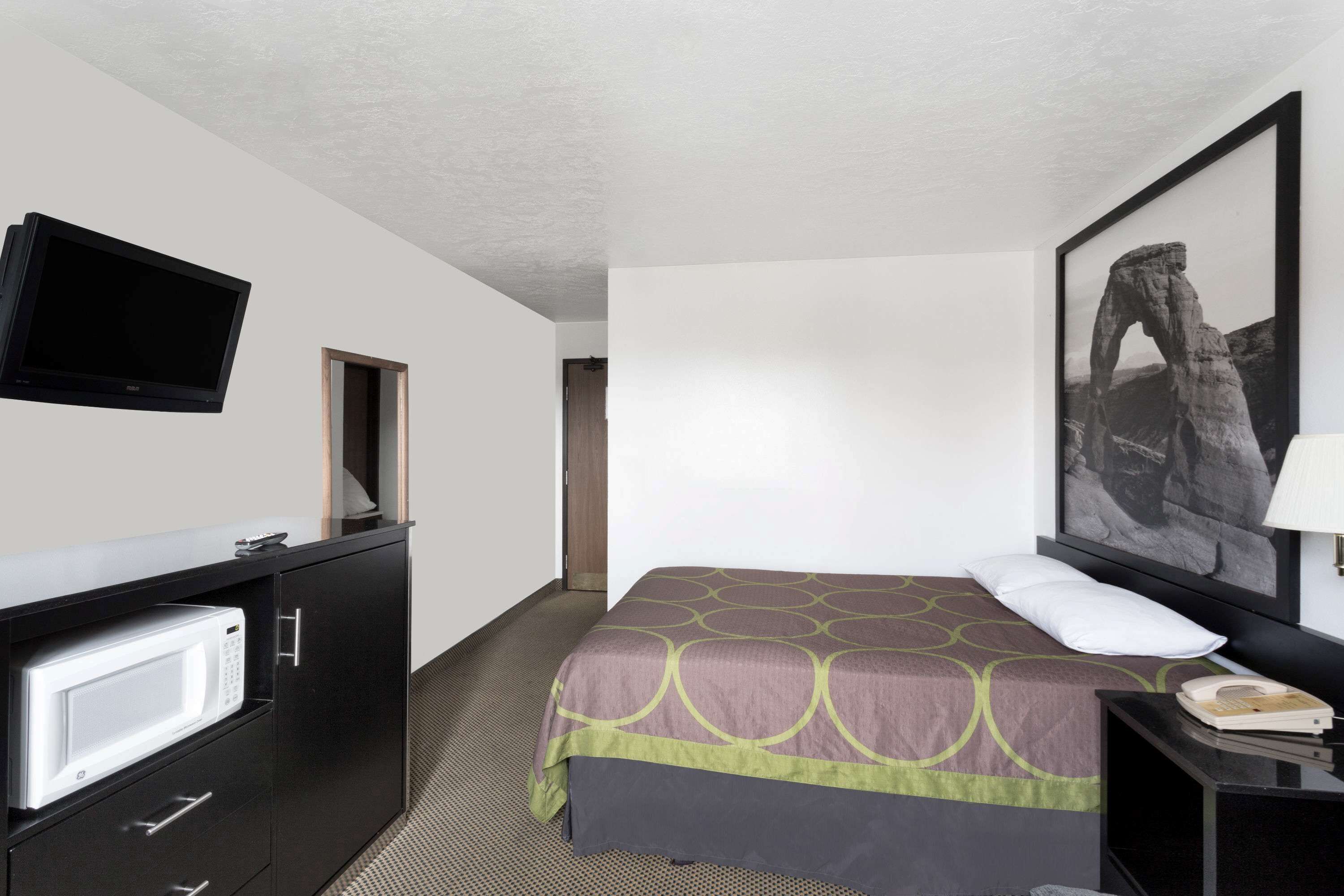 Una habitación de hotel con cama, televisión montada en la pared, escritorio con teléfono y un cuadro enmarcado.