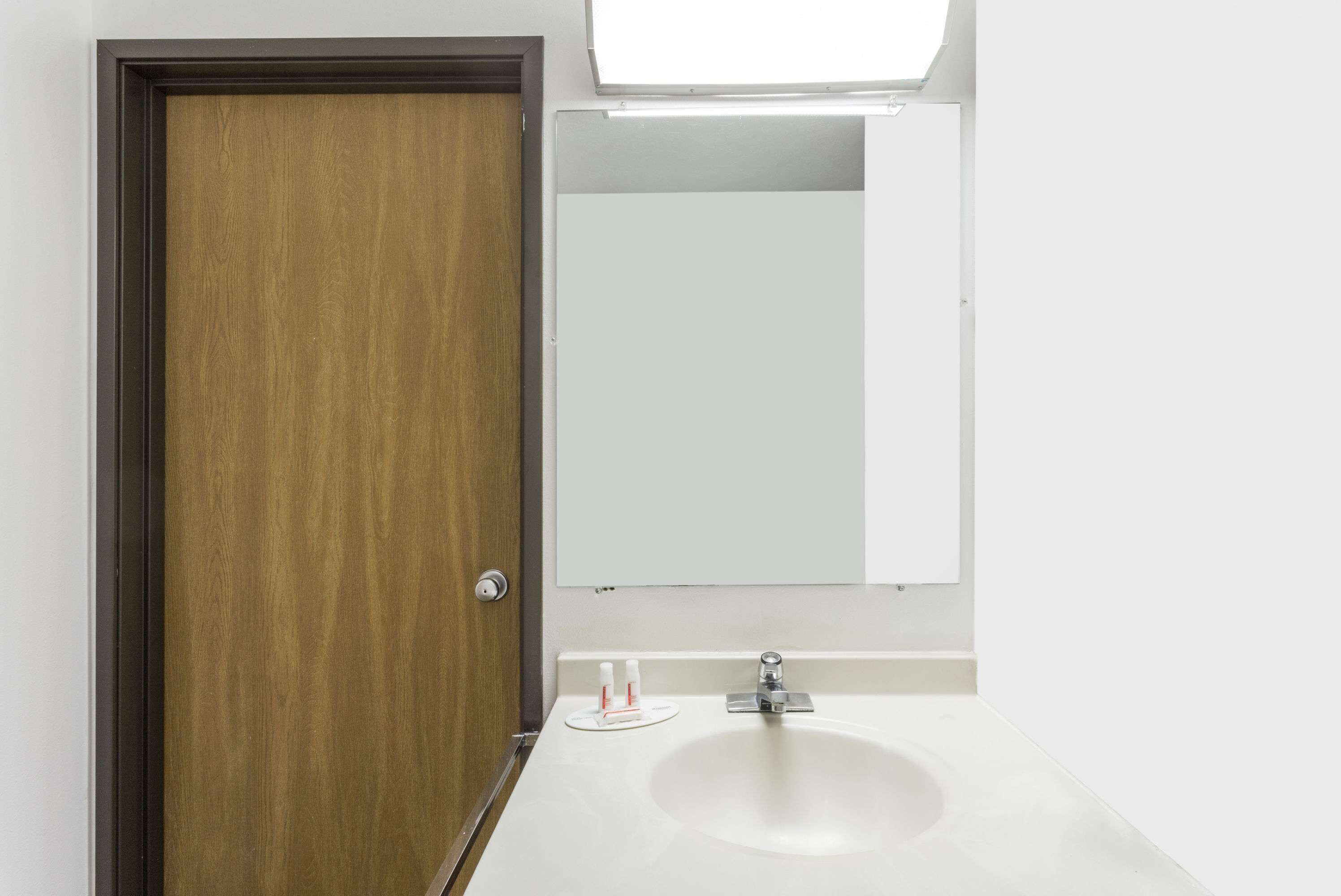 A bathroom with a wooden door, a white sink, and a mirror above it.