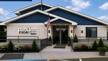 A Park Inn hotel with a modern design, featuring a flag, a signboard, and a well-maintained entrance area.