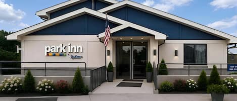 A Park Inn hotel with a modern design, featuring a flag, a signboard, and a well-maintained entrance area.