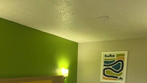 A hotel room with a bed, a nightstand, a lamp, and a wall art piece. - Park Inn by Radisson (Coraopolis)