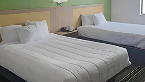 Quarto de hotel com duas camas, uma mesinha de cabeceira e uma luminária na parede.