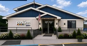 Un hotel Park Inn con diseño moderno, que presenta una destacada bandera estadounidense, una entrada acogedora y jardines bien cuidados.