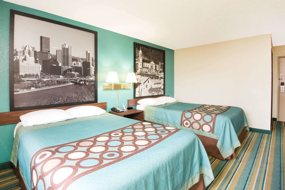 A hotel room with two beds, a cityscape poster, a lamp, and a striped carpet.