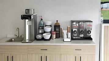 A kitchen counter with a coffee maker, a kettle, a coffee grinder, a toaster, and a coffee machine.