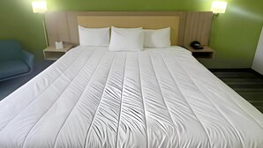 Quarto de hotel com cama grande, duas luminárias de cabeceira, mesa de cabeceira e uma cadeira azul.