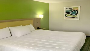 Quarto de hotel com uma cama, mesa de cabeceira, abajur e uma parede com um quadro emoldurado.