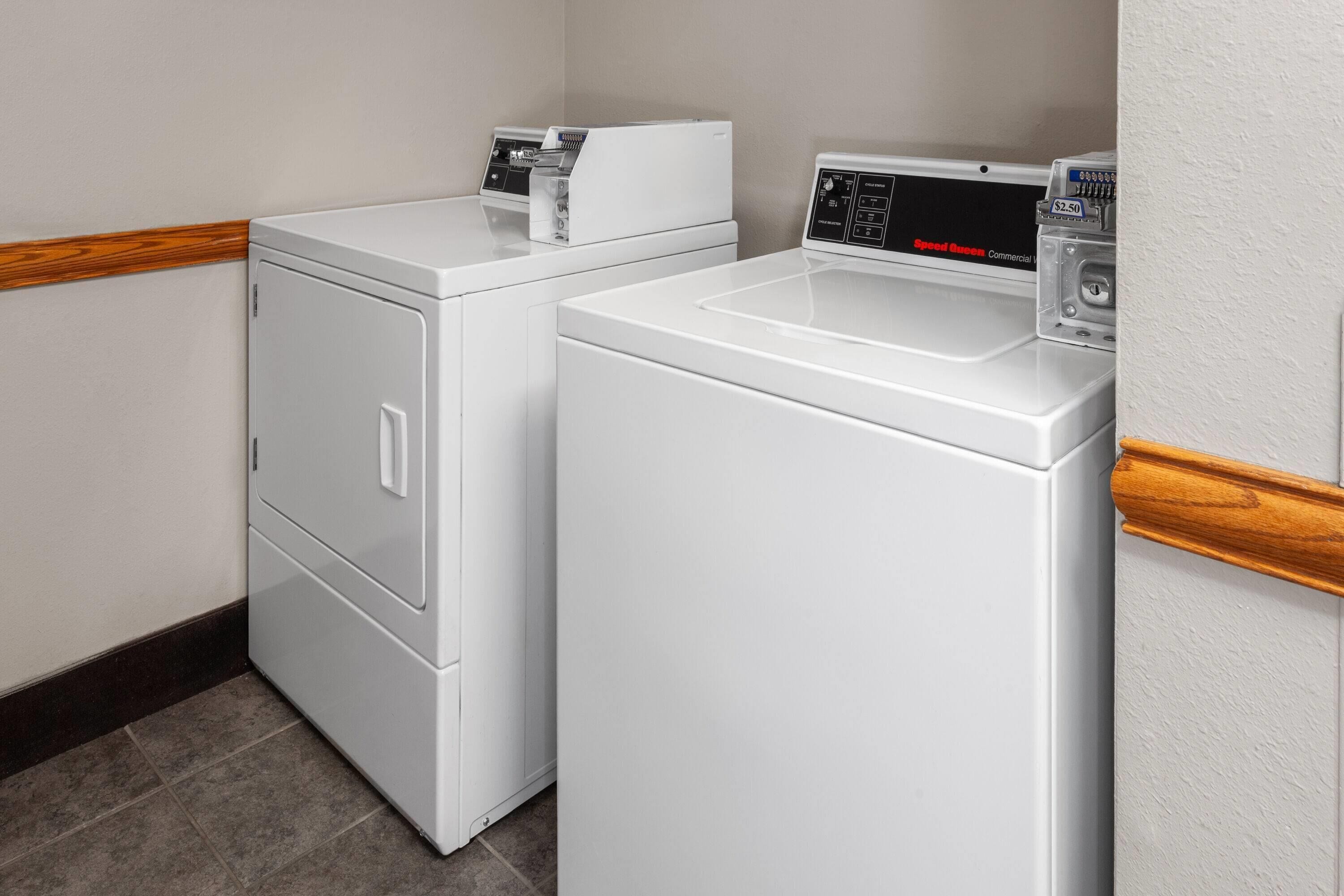 A laundry area with two white washing machines and a dryer, wooden trim along the walls, and a tiled floor.