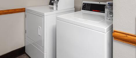 A laundry area with two white washing machines and a dryer, wooden trim along the walls, and a tiled floor.