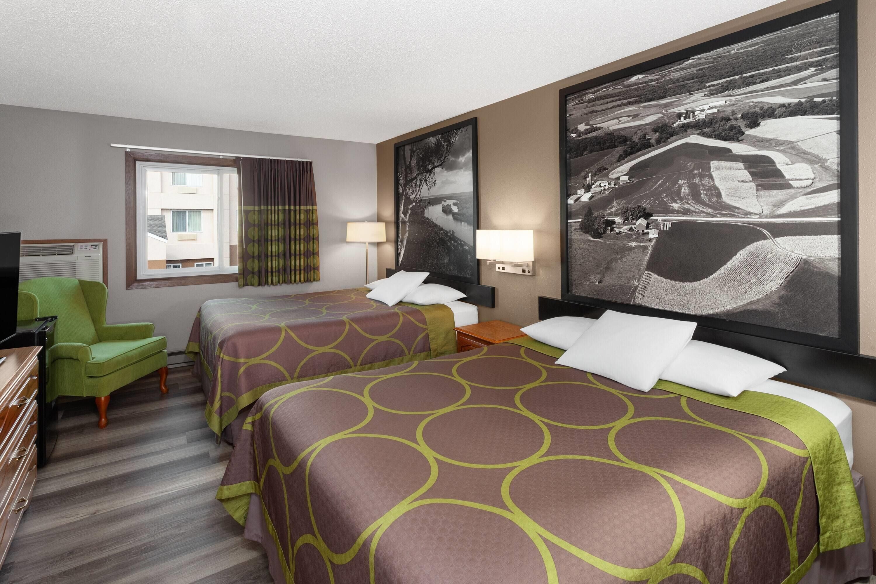 A hotel room with two beds, a desk, a chair, and a large framed picture on the wall.