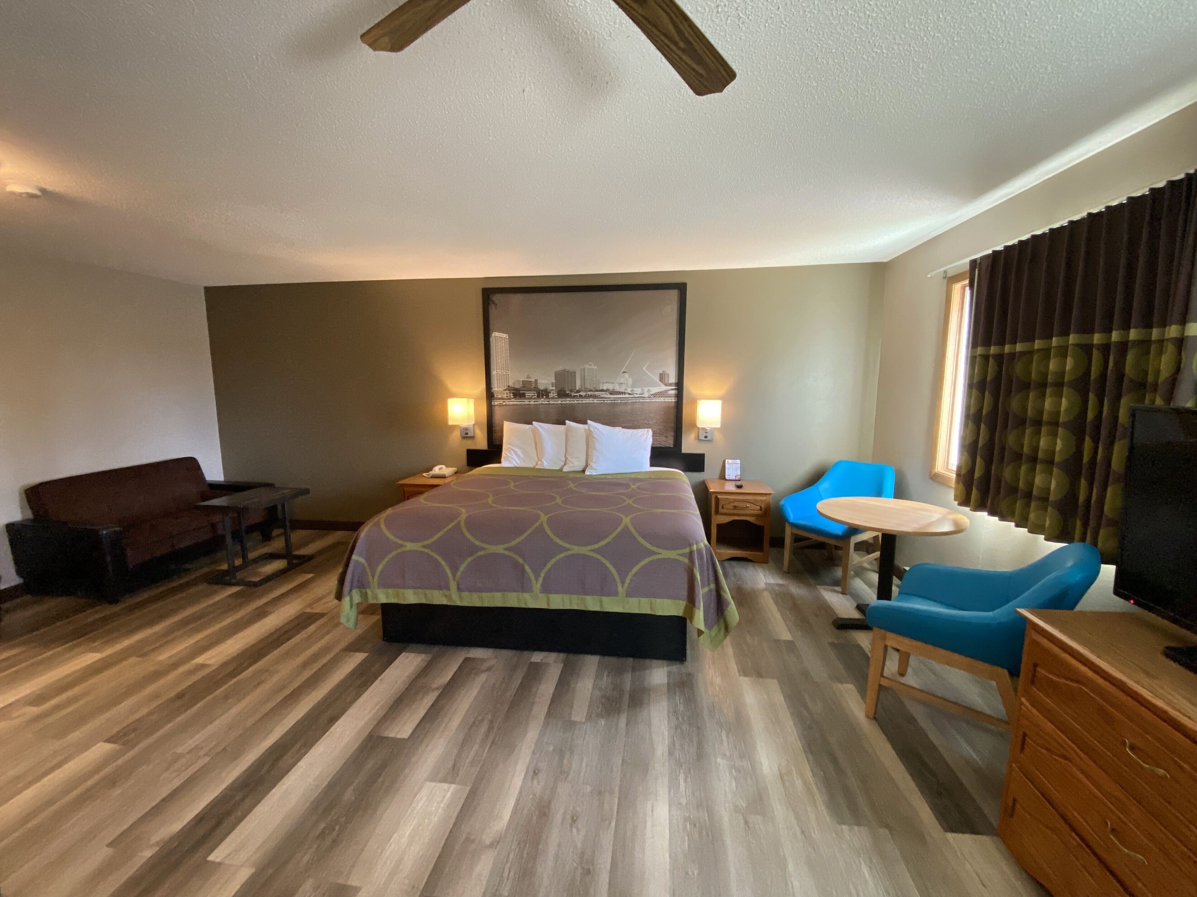 A hotel room with a large bed, a desk, a chair, a TV, and a window with curtains.