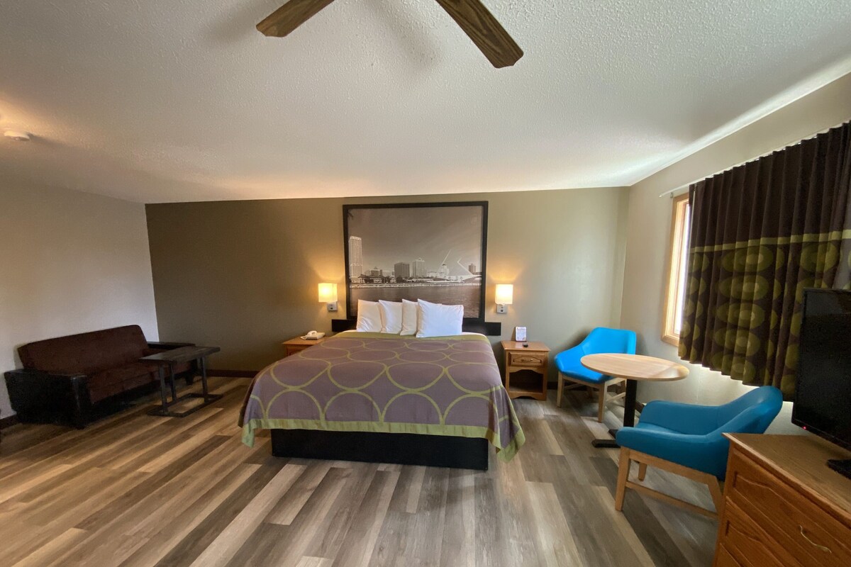 A hotel room with a large bed, a desk, a chair, a TV, and a window with curtains.