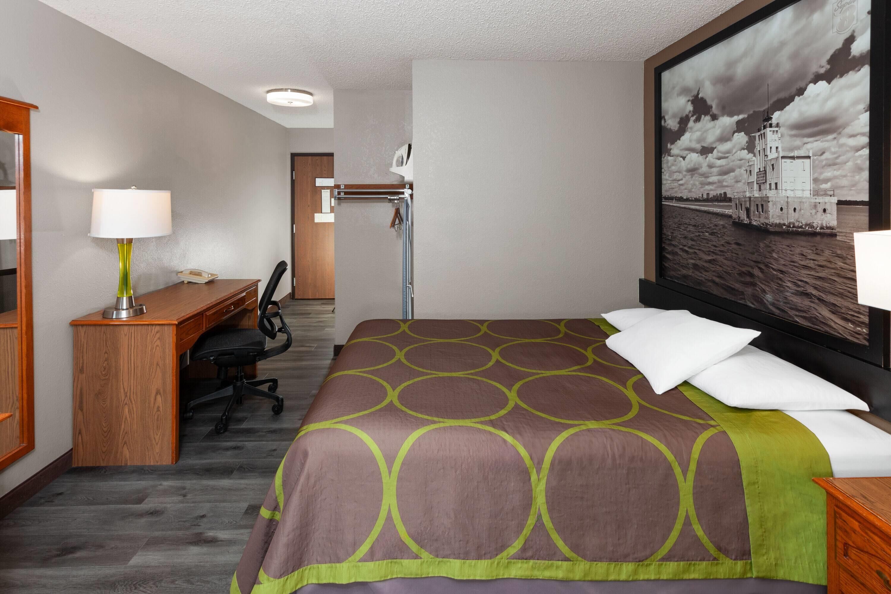Una habitación de hotel con cama, escritorio, silla y un cuadro grande de un faro.