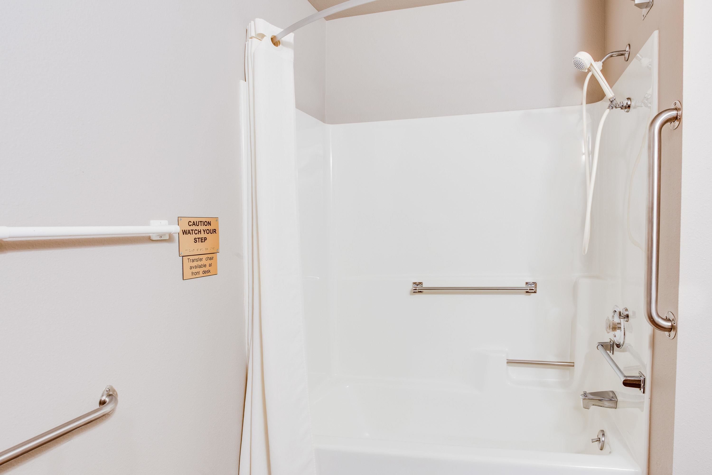 A bathroom with a white bathtub, grab bars, a showerhead, and a caution sign.