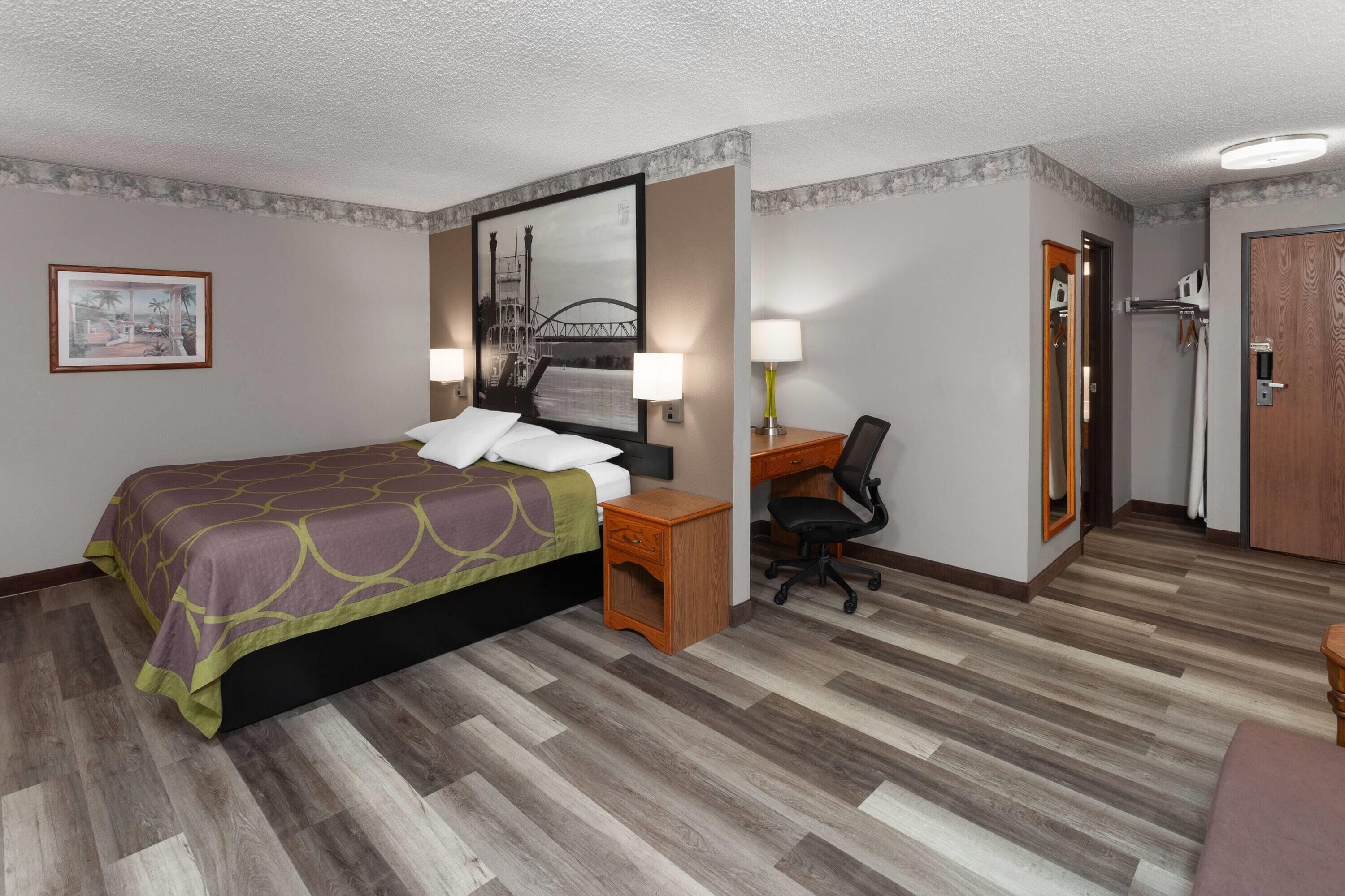 A hotel room with a bed, desk, chair, and a mirror.