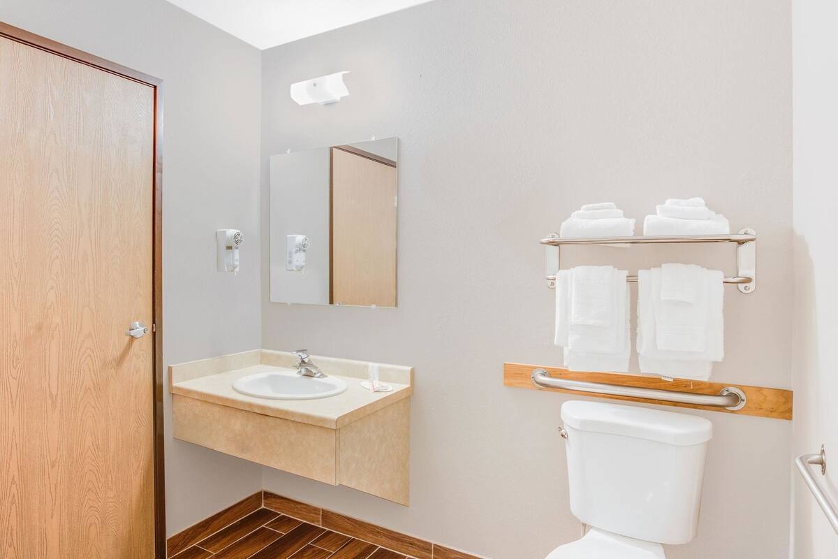 Un baño con puerta de madera, un lavabo con espejo, un inodoro con toallero y un secador de manos.
