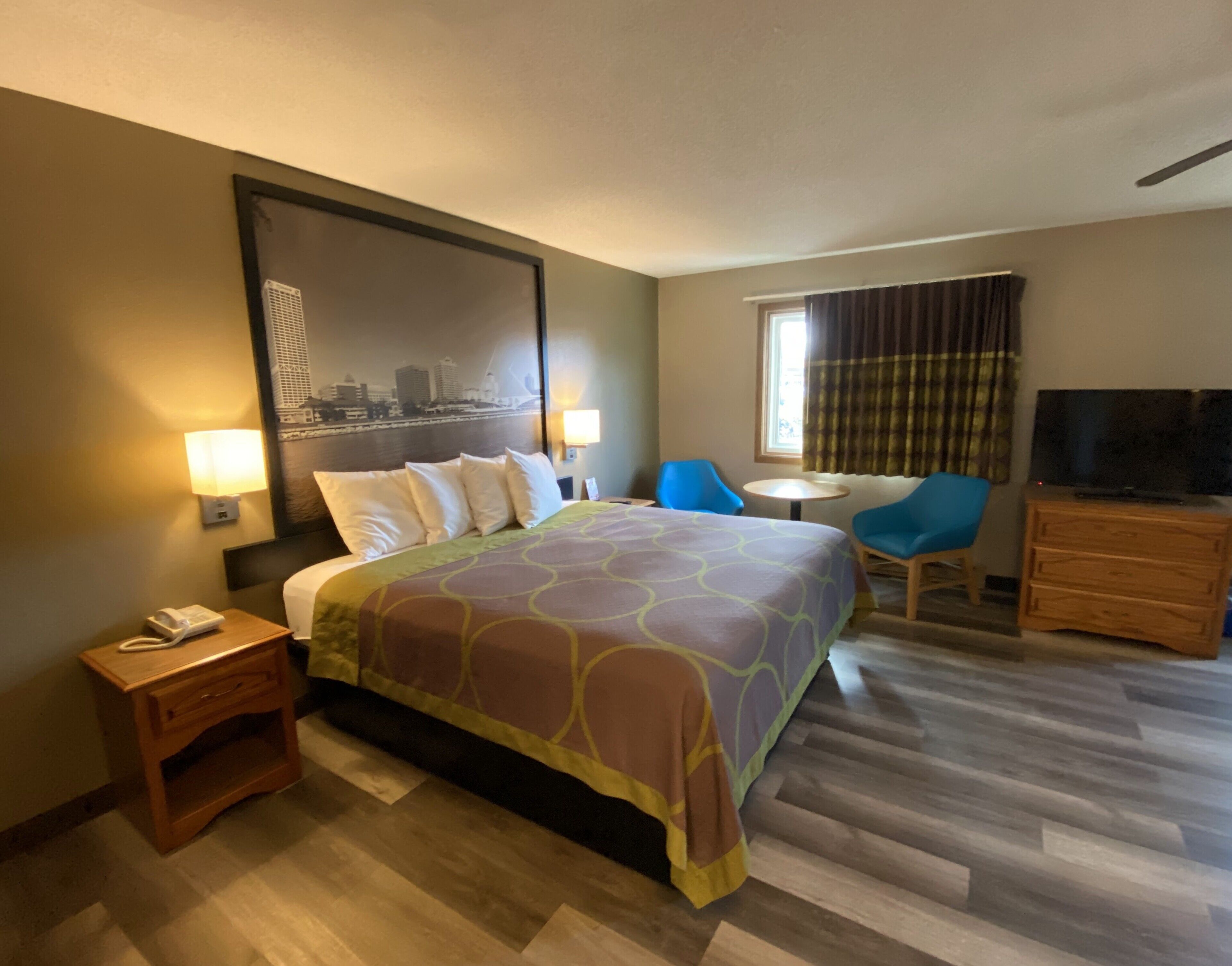 Une chambre d’hôtel avec un grand lit, un bureau avec un téléphone, une chaise, une télévision et une fenêtre avec des rideaux.