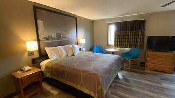 A hotel room with a large bed, a desk with a telephone, a chair, a television, and a window with curtains.