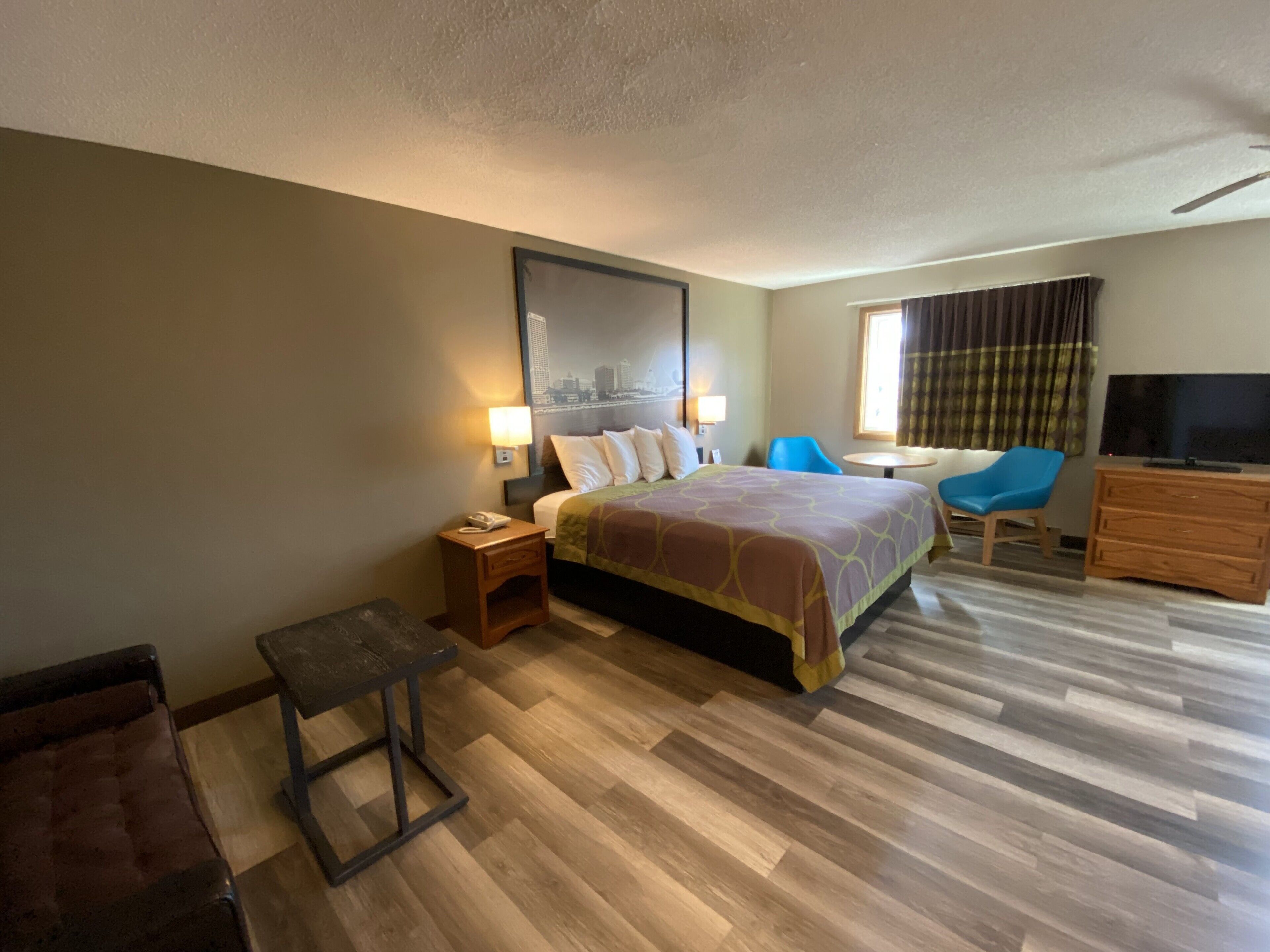 A hotel room with a bed, a desk, a chair, a TV, and a window with curtains.