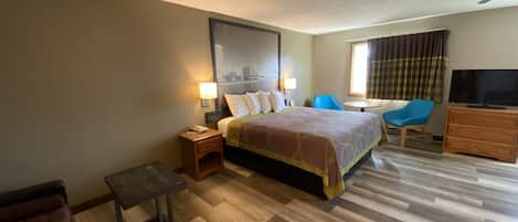 A hotel room with a bed, a desk, a chair, a TV, and a window with curtains.