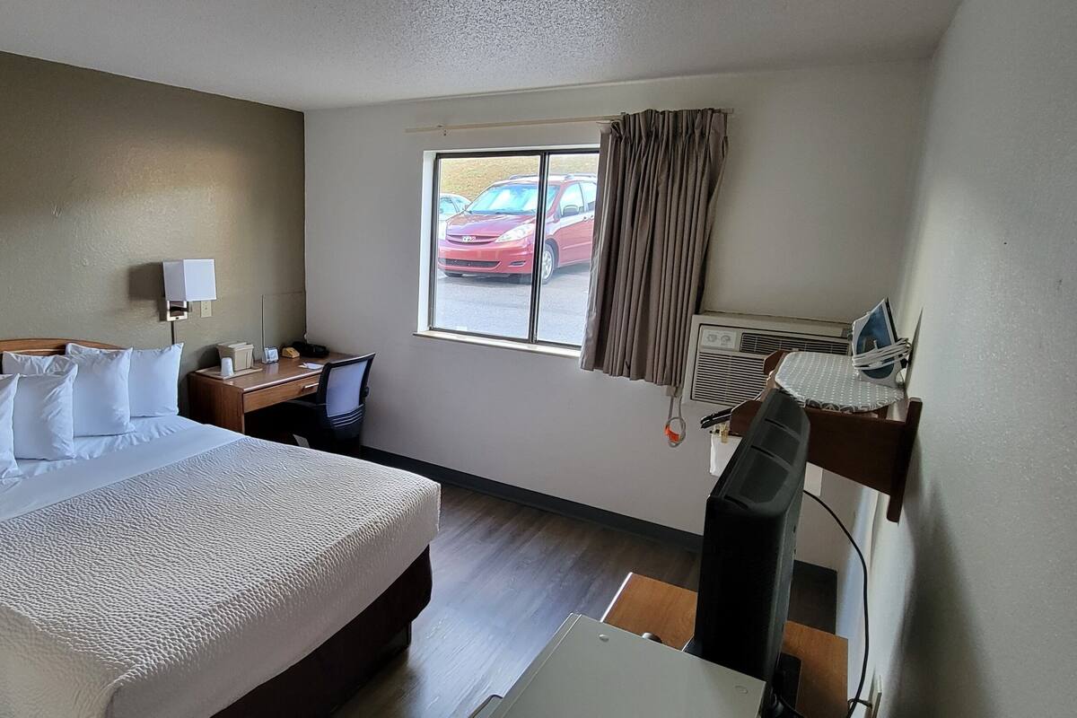 Een hotelkamer met een bed, nachtkastje, lamp, raam en airconditioning.