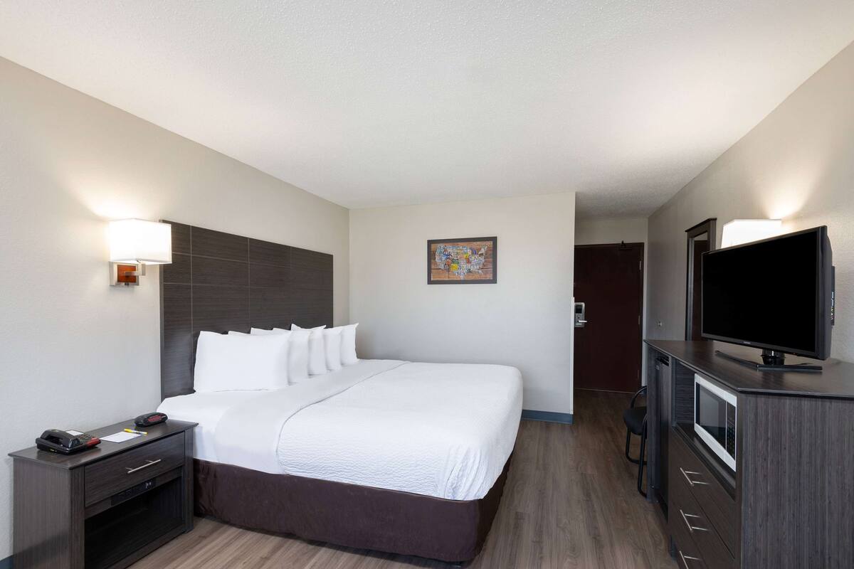 Een hotelkamer met een groot bed, een nachtkastje met een lamp, een televisie en een klein bureau met stoel.
