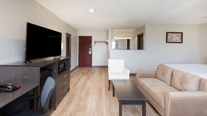 A modern hotel room with a flat-screen TV, a sofa, a dining table, and a kitchen area with a microwave.