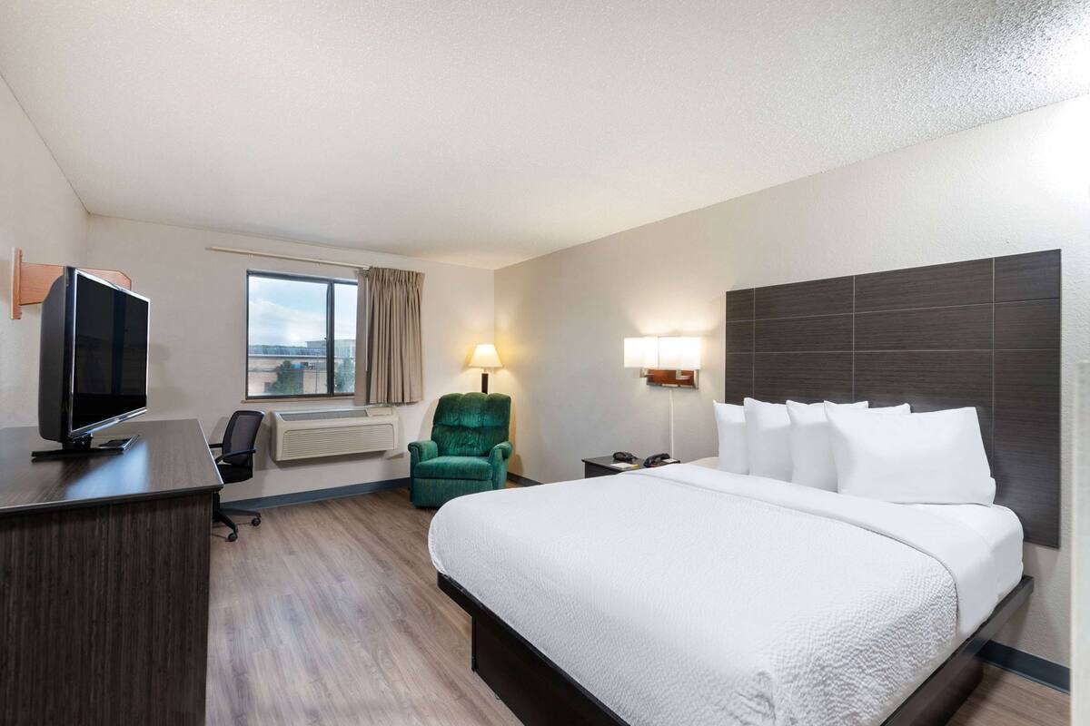 Een hotelkamer met een bed, een bureau met een televisie, een stoel, een lamp en een raam.