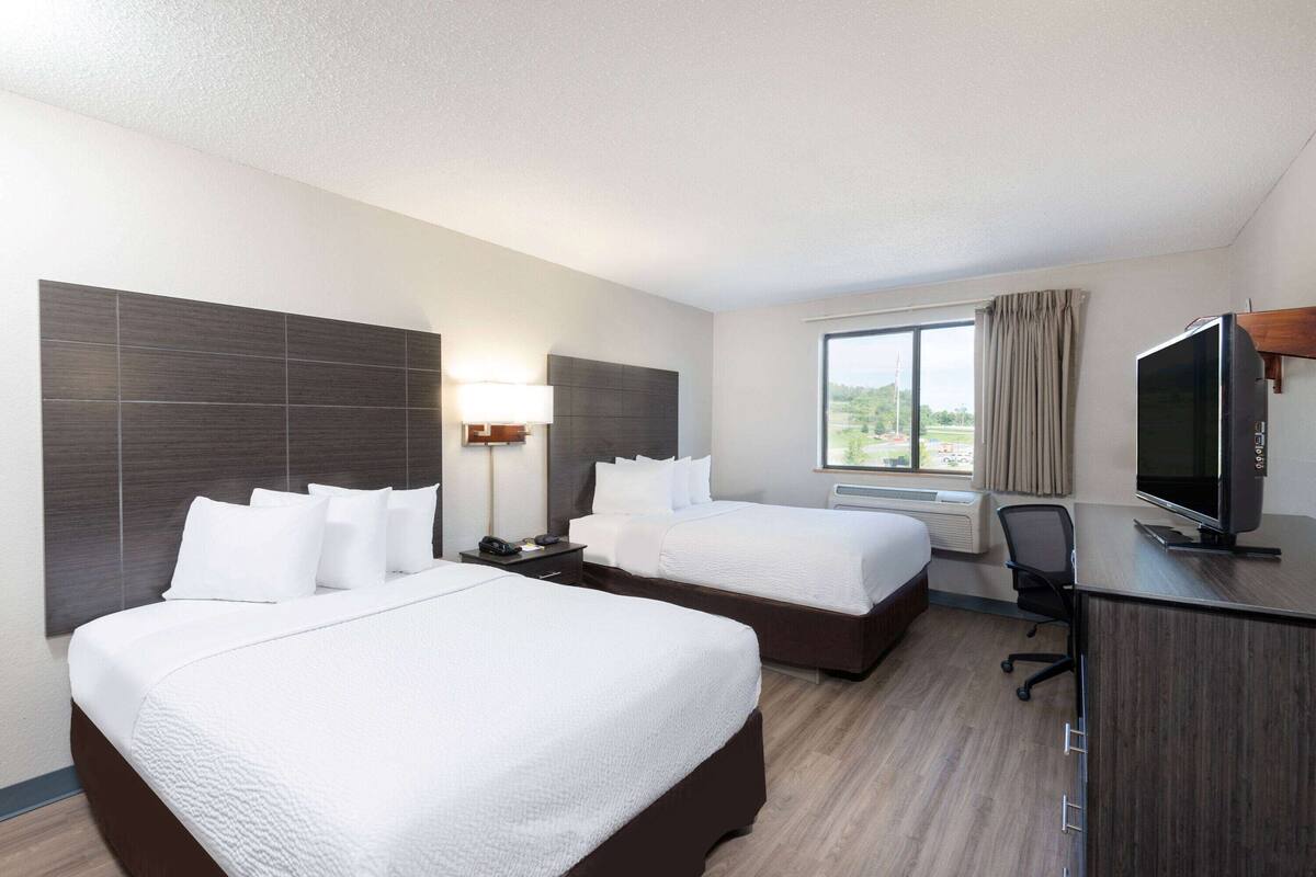 Een hotelkamer met twee bedden, een bureau, een televisie en een raam met gordijnen.