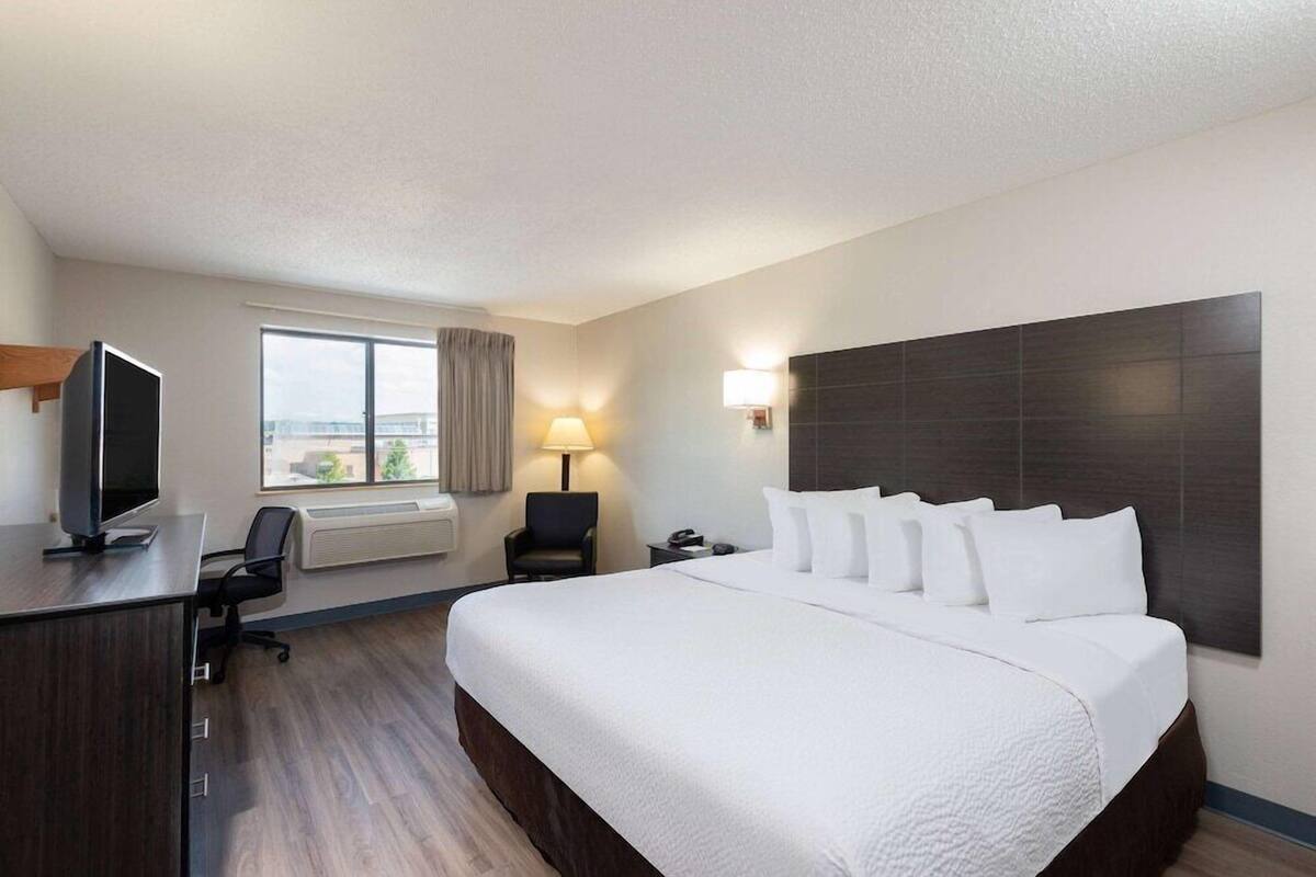 Een hotelkamer met een groot bed, een bureau met een televisie, een stoel, een lamp en een raam met uitzicht.