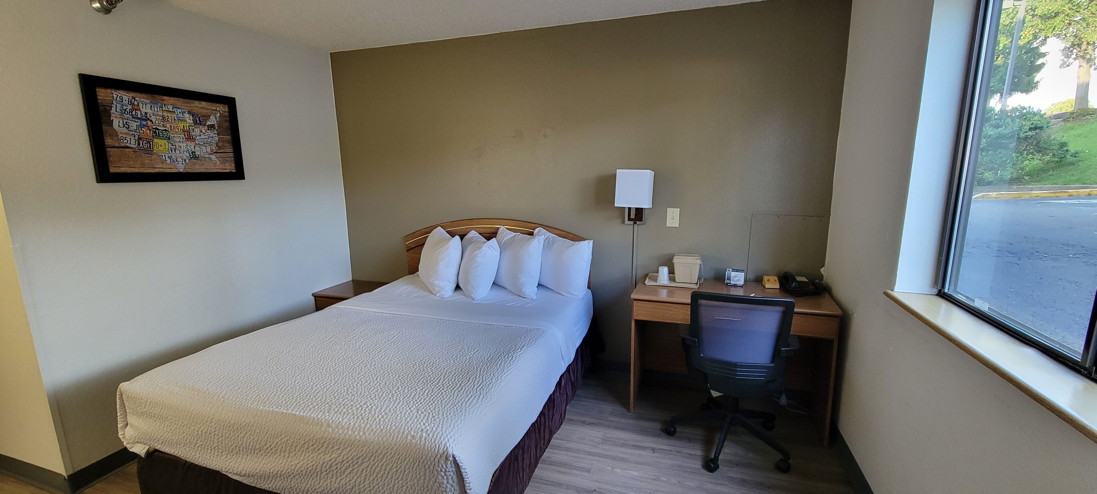 A hotel room with a bed, a desk, a chair, a lamp, and a window.