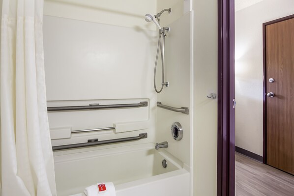 A bathroom with a white bathtub, grab bars, and a shower head.