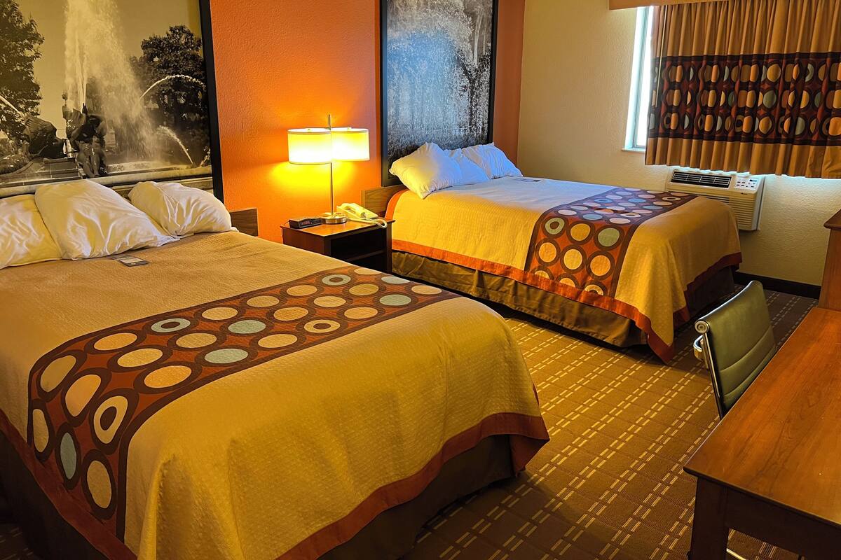 Habitación de hotel con dos camas, una mesita de noche con lámpara, un cuadro en la pared y una ventana con cortinas.