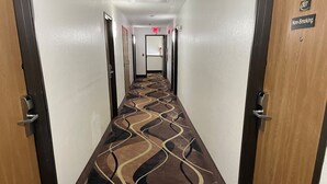 Ein Hotelgang mit Teppichmuster, Türen auf beiden Seiten und einem Rauchverbotsschild an der rechten Wand.