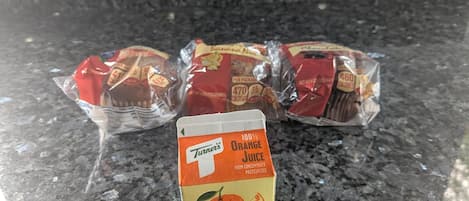 A carton of orange juice and several packages of banana and apple juice on a granite countertop.