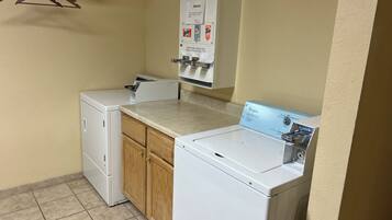 A laundry area with two washers and dryers, wooden cabinets, and a bulletin board with laundry detergent ads.