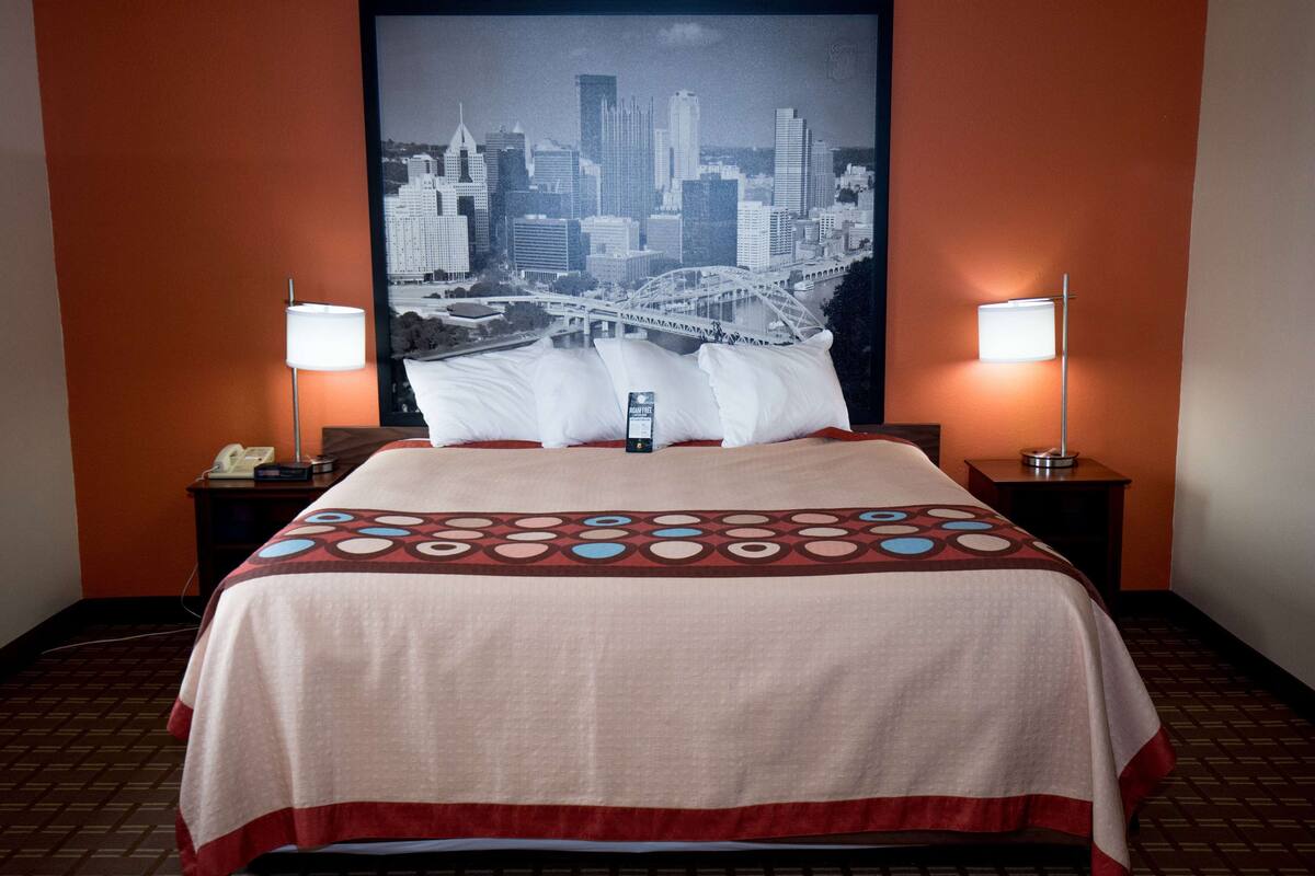 Una habitación de hotel con cama, dos mesitas de noche con lámparas, un cartel con vista a la ciudad en la pared y una colcha estampada.