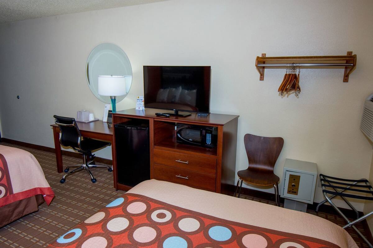 Habitación de hotel con cama, escritorio con televisor, microondas, silla, caja de seguridad pequeña y perchero.