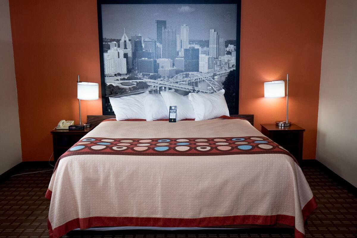 Habitación de hotel con cama, dos lámparas de noche, un cartel con vista urbana y un teléfono en la mesita de noche.