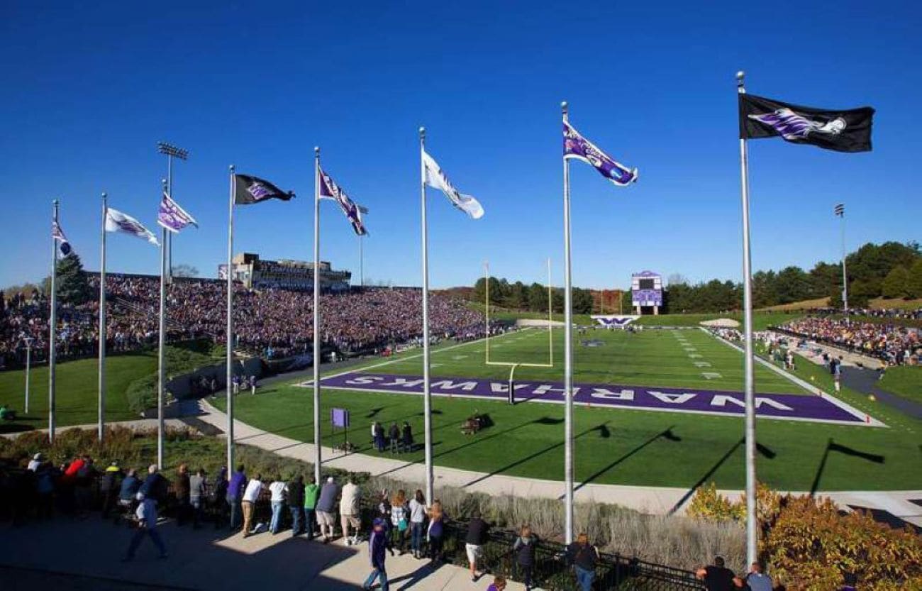 A stadium with multiple flags, a football field, and a crowd of spectators.