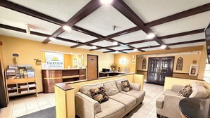 A hotel reception area with a reception desk, a sofa, a chair, and a coffee table. There are signs on the wall and a clock. - Fairview Inn & Suites Whitewater (Whitewater)