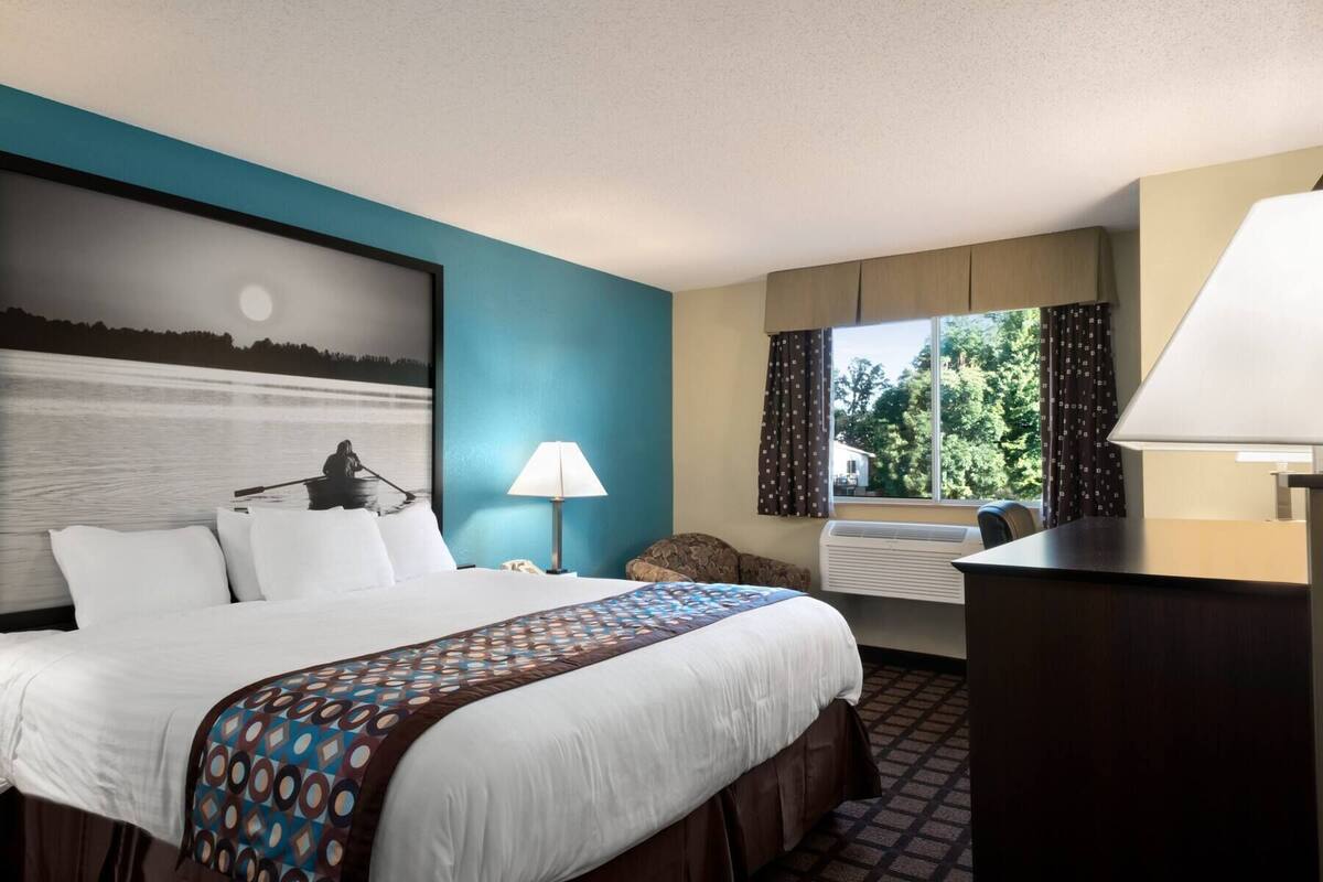 A hotel room with a large bed, a desk, a lamp, and a window with curtains.