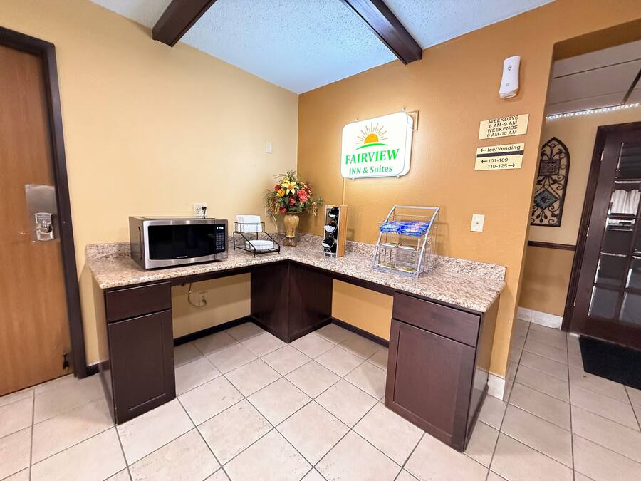 A hotel reception area with a microwave, a coffee machine, and a flower vase on the counter.