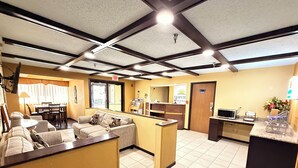 A hotel lobby with a reception desk, a seating area with couches, a dining table, and a kitchen area with a microwave. - Fairview Inn & Suites Whitewater (Whitewater)