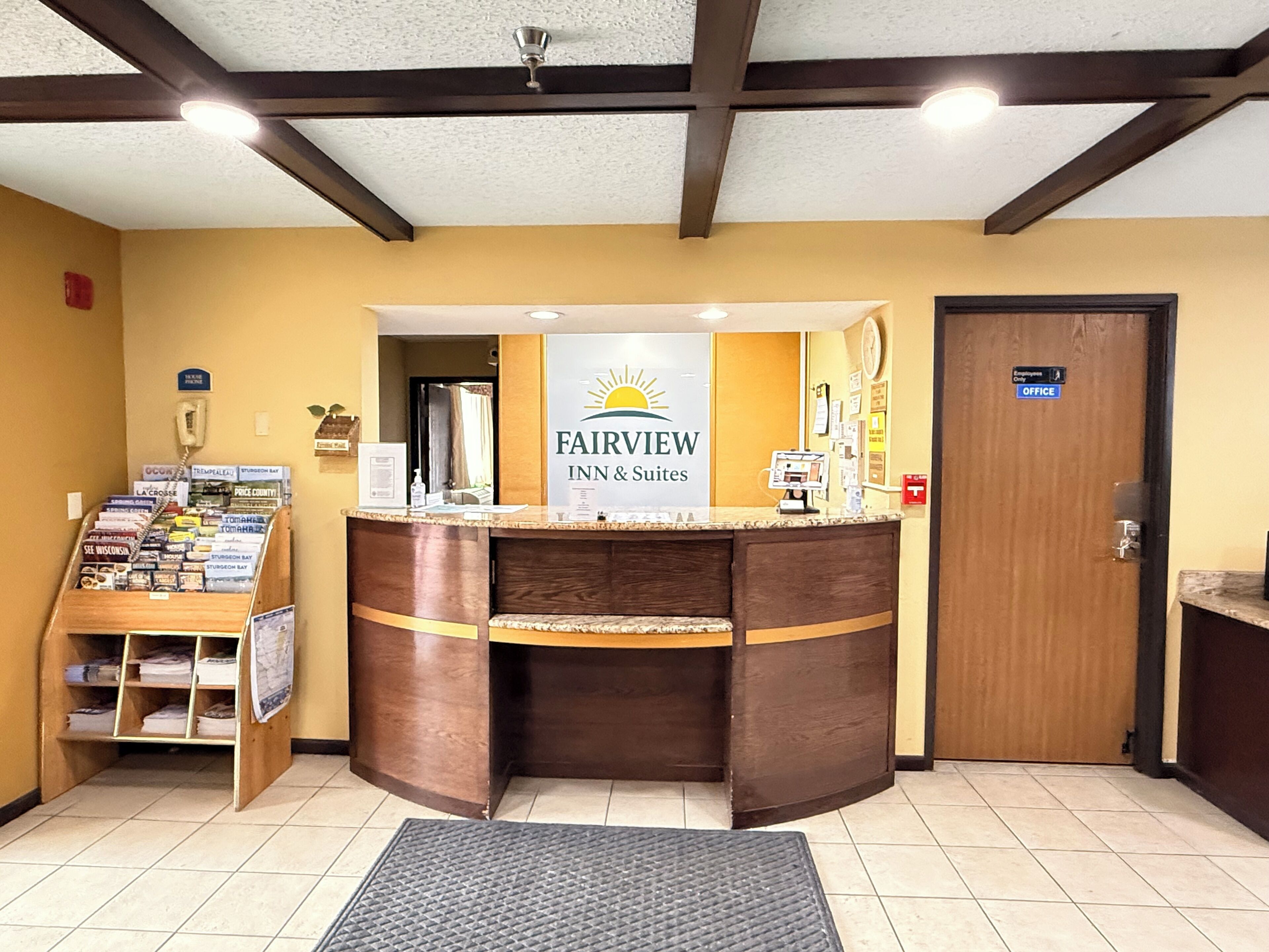 A reception desk with a sign for Fairview Inn & Suites, a phone, a small desk with a computer, a bulletin board with various notices, and a door labeled "Employee Only".