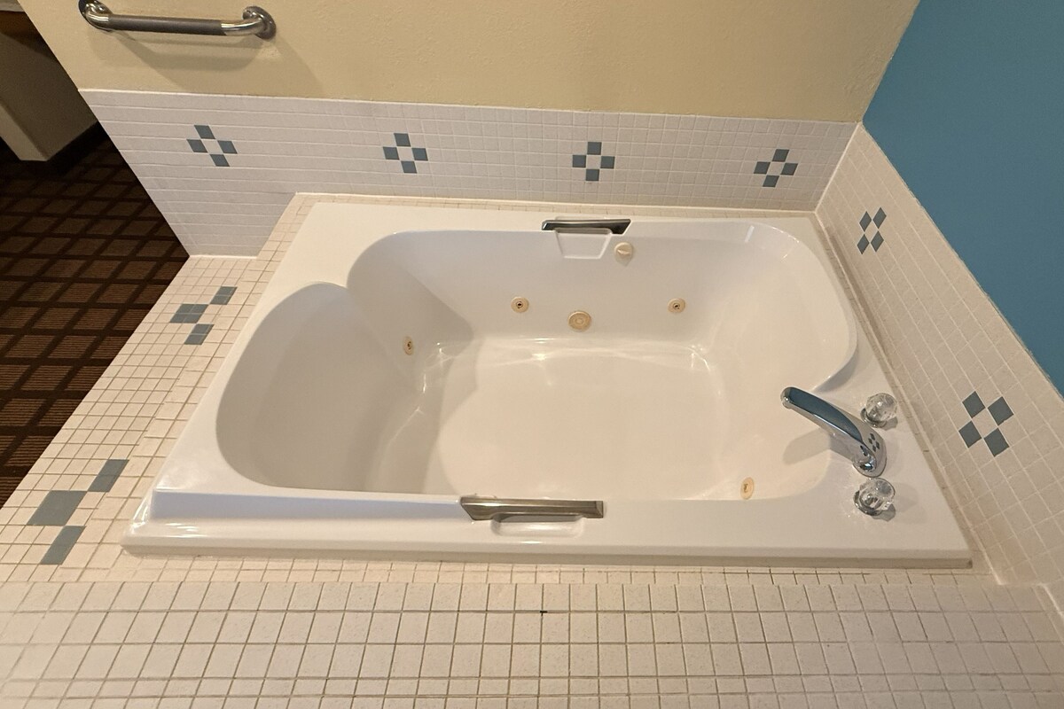A standard bathtub with a handheld showerhead, a built-in seat, and a faucet.