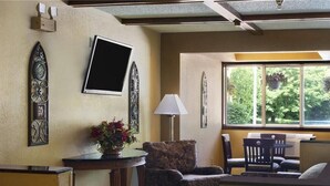 A living room with a sofa, chairs, a table with a vase of flowers, a lamp, and a large window with a view of trees. - Fairview Inn & Suites Whitewater (Whitewater)